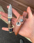 Damascus antler hunting knife with custom blade and leather sheath, featuring a detailed Damascus pattern and antler handle.