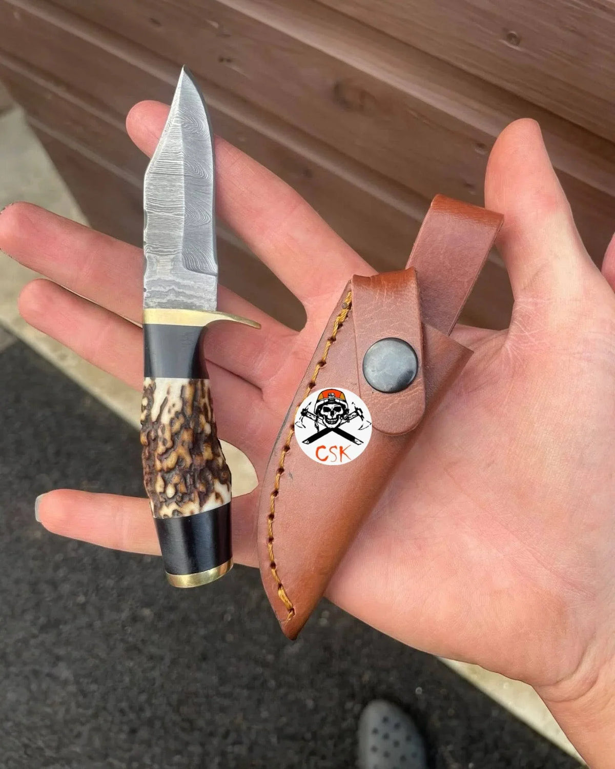 Damascus antler hunting knife with custom blade and leather sheath, featuring a detailed Damascus pattern and antler handle.