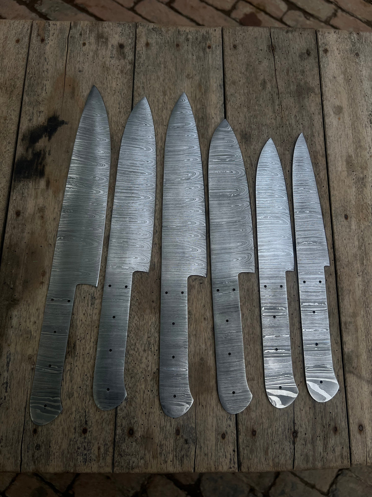 Six handmade Damascus chef knives with forged steel blades, displayed together as a custom knife making supply by JW SteelCrafts.