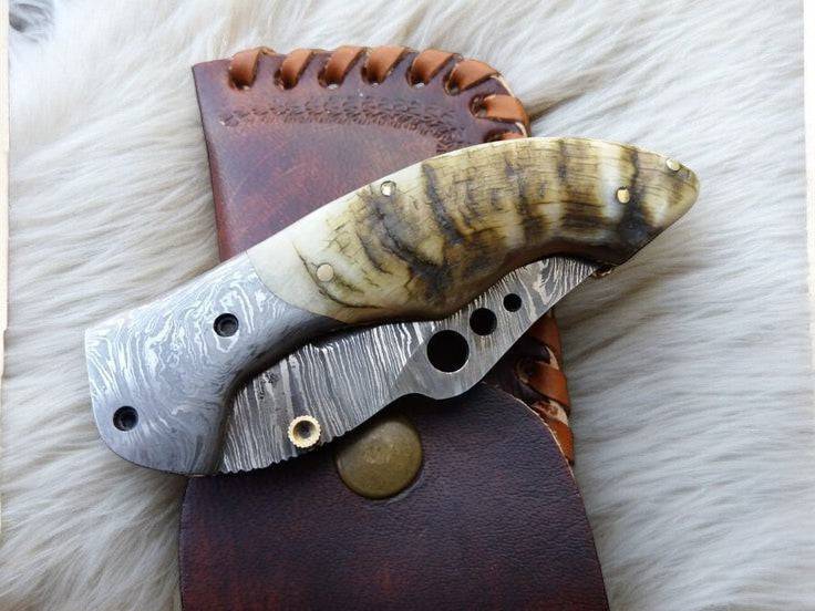 Handmade Damascus pocket knife with sheep horn handle and intricate blade design, crafted for everyday carry and precision cutting.