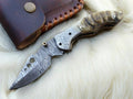 Handmade Damascus pocket knife with sheep horn handle, showcasing intricate blade design and natural horn handle detail.