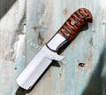 Handmade 7-inch cowboy bull cutter knife by CSK Forged with leather sheath, featuring a sharp stainless steel blade and rustic handle.