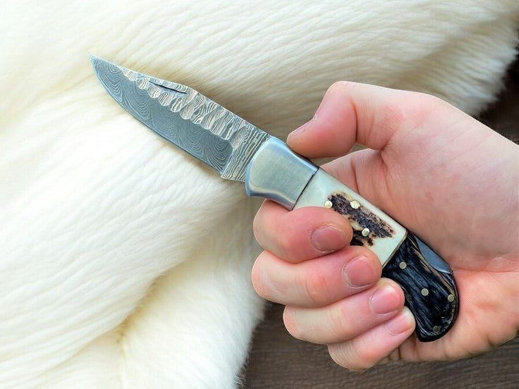 Handmade Damascus folding knife with stag horn handle and rosewood accents, featuring a sharp blade and detailed craftsmanship.