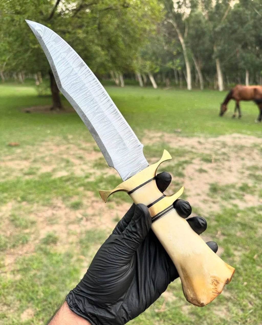 Handmade 16-inch Damascus steel Bowie knife with brass guard, camel bone handle, and leather sheath by Knives Gear Garage.