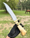 Handmade 16-inch Damascus steel Bowie knife with brass guard, camel bone handle, and leather sheath by Knives Gear Garage.