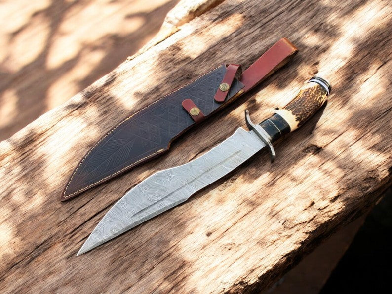 Handmade Damascus Bowie knife with antler horn handle and intricate blade design, crafted for durability and style.