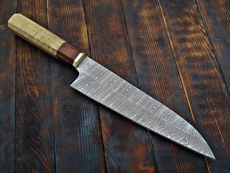 Custom handmade Damascus chef knife with intricate layered blade and wooden handle from Knives Gear Garage, displayed on a wooden surface.