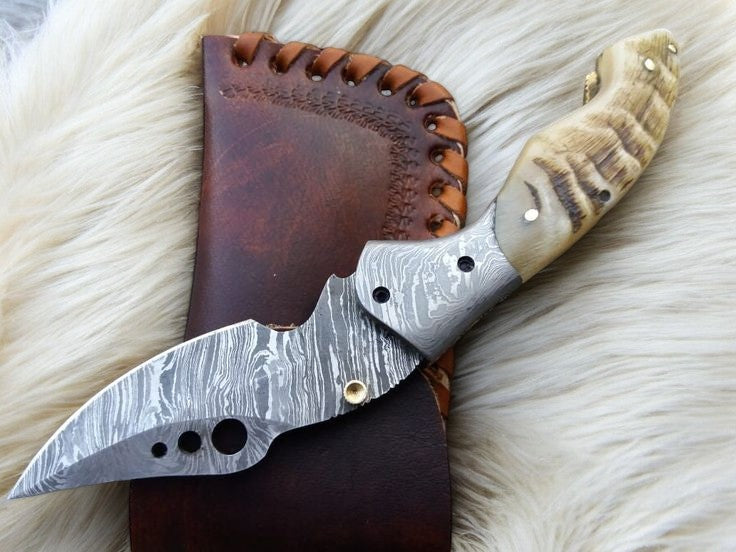 Handmade Damascus pocket knife with a sheep horn handle, featuring intricate blade patterns and a compact, traditional design.