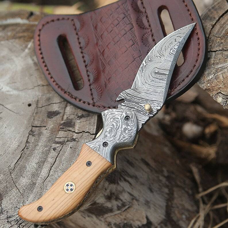 Damascus pocket knife by Knives Gear Garage with a patterned blade and wooden handle, open to show its sharp edge.