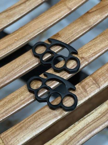 Pair of black hand-casted knuckles from CSK Forged, showcasing durable, detailed metal craftsmanship in a close-up view.