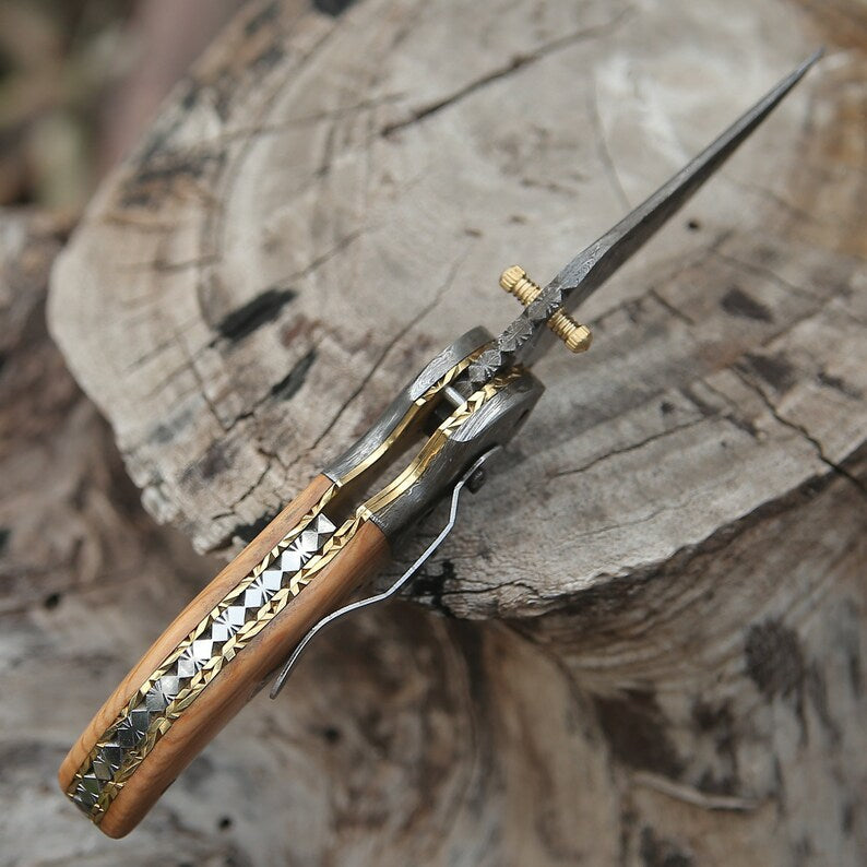 Damascus pocket knife by Knives Gear Garage with intricate layered blade and ergonomic handle, open on a wooden surface.
