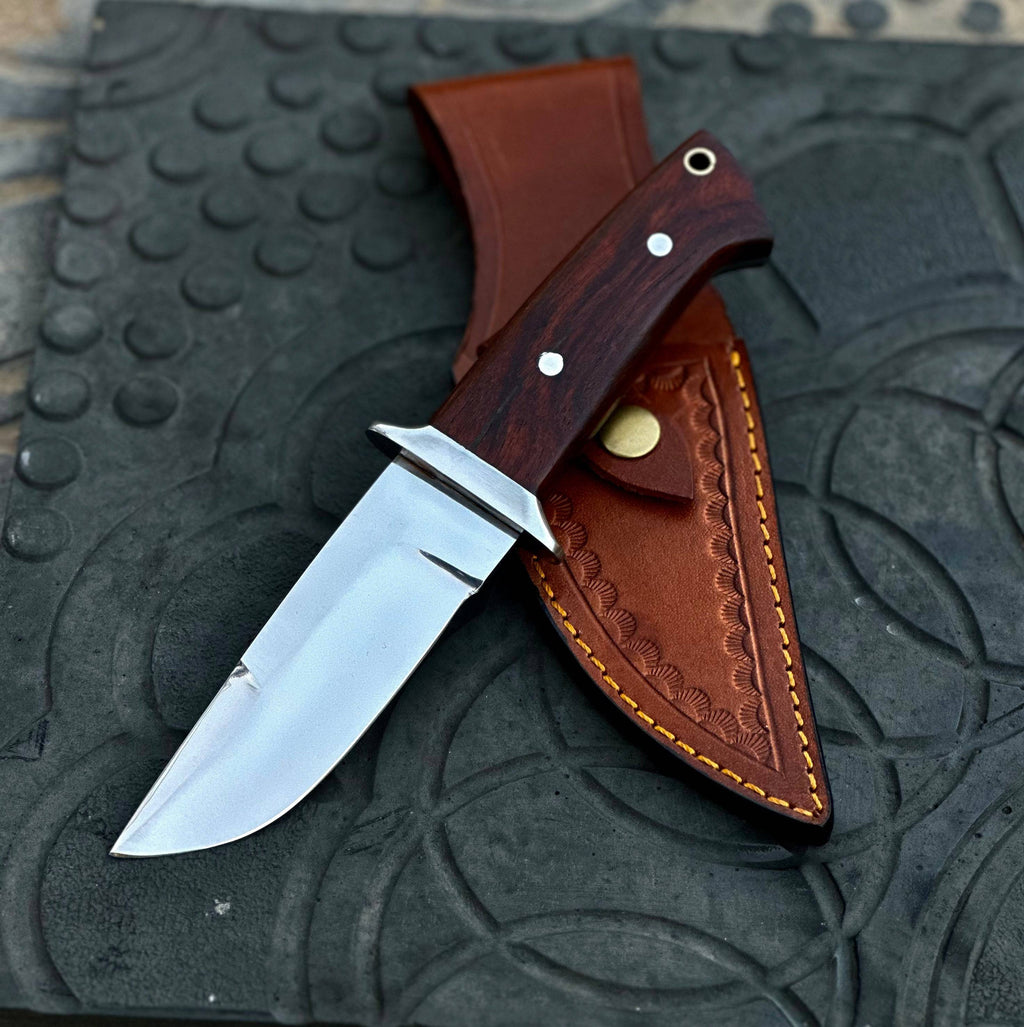 Handmade 1095 steel hunting knife with a wooden handle and leather sheath, crafted by Knives Gear Garage.