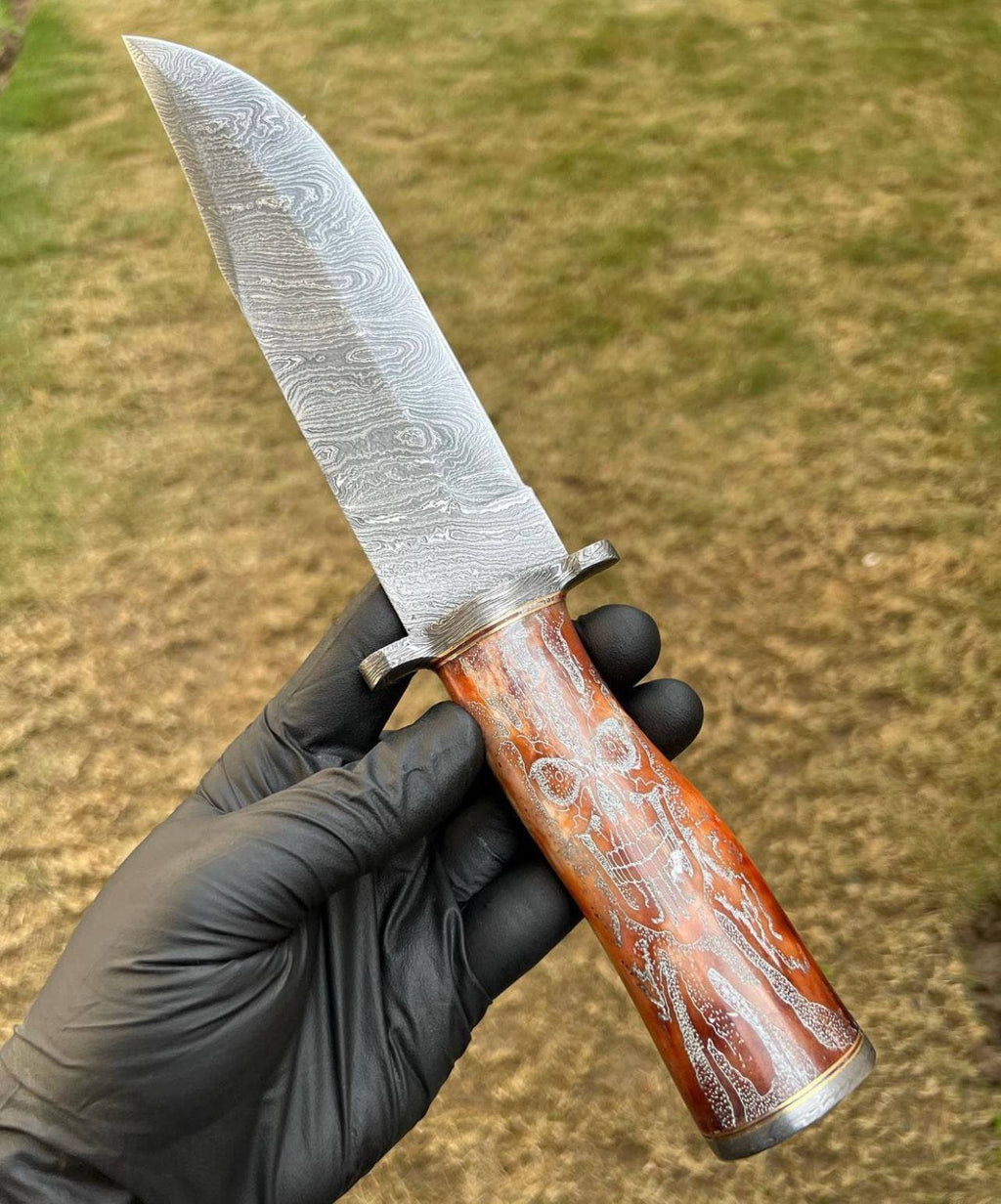 Handmade Damascus hunting knife with skull handle by cskforged, featuring a sharp blade and detailed handle for outdoor use.