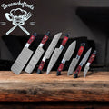 Handmade Damascus steel kitchen knives set with Pakkawood handles, steel bolster, and leather sheath, displayed on a wooden surface.