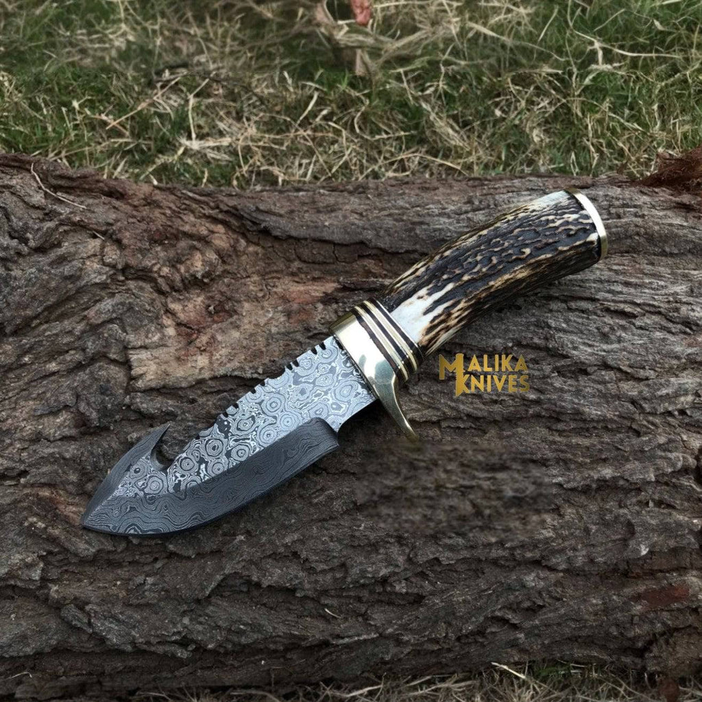 Damascus gut hook skinning knife with stag horn handle by Malika Knives, featuring a sharp curved blade for field dressing game.