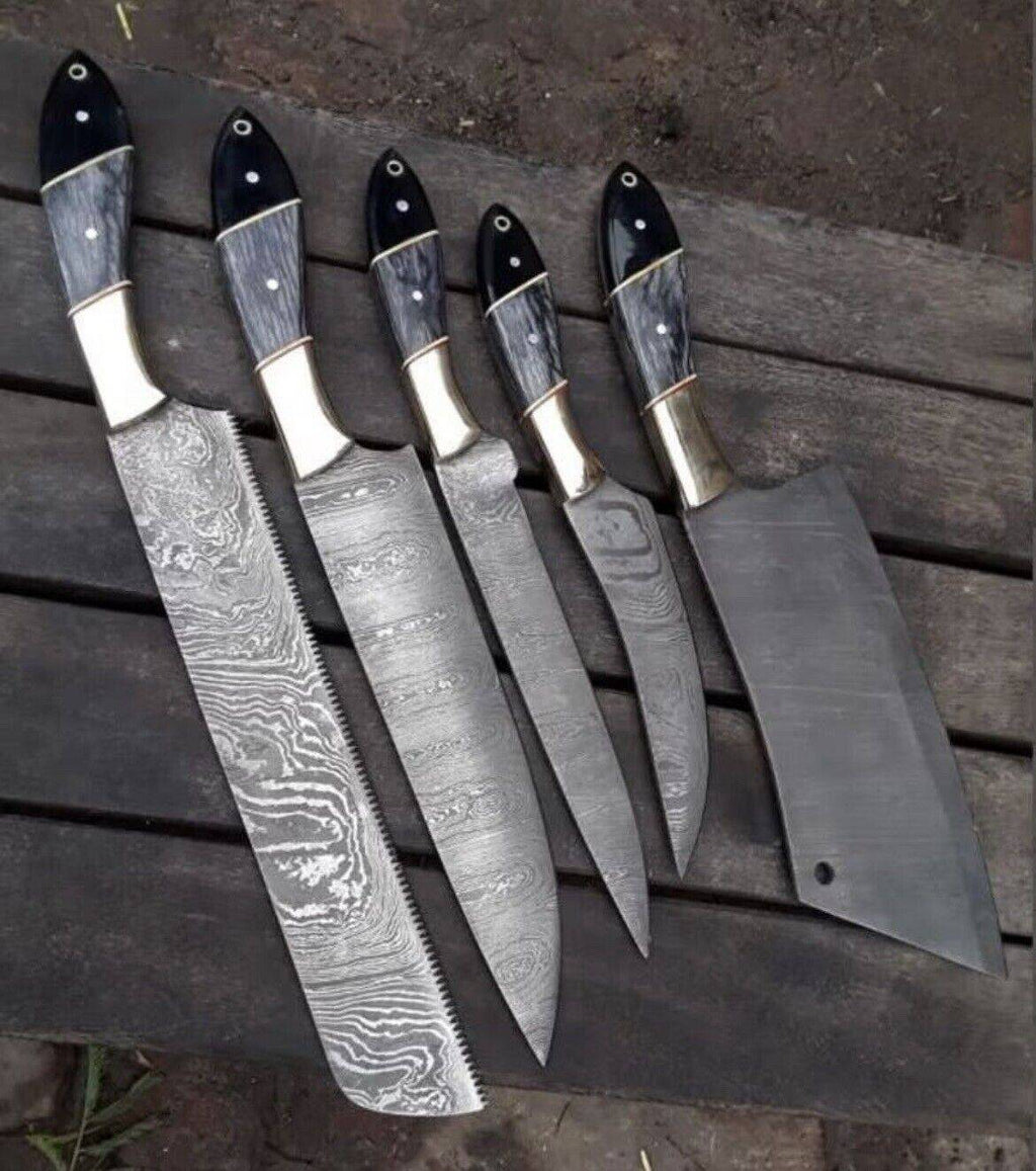 Custom handmade Damascus steel kitchen knives set with pakkawood and buffalo horn handles, resting in a leather sheath.