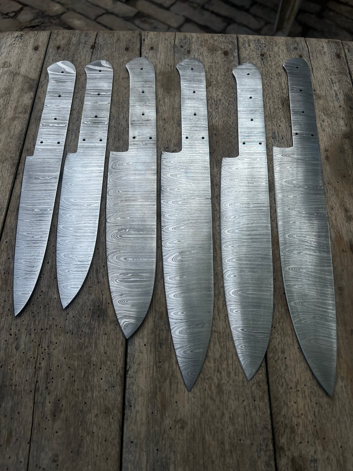 Six handmade Damascus chef knives with forged steel blades from JW SteelCrafts, displayed on a wooden surface.
