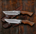 Handmade hunting knife with wooden handle and sharp stainless steel blade, displayed on a wooden surface.
