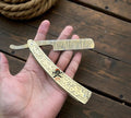 Damascus steel straight razor with engraved brass handle, handmade barber razor by cskforged, displayed on a wooden surface.