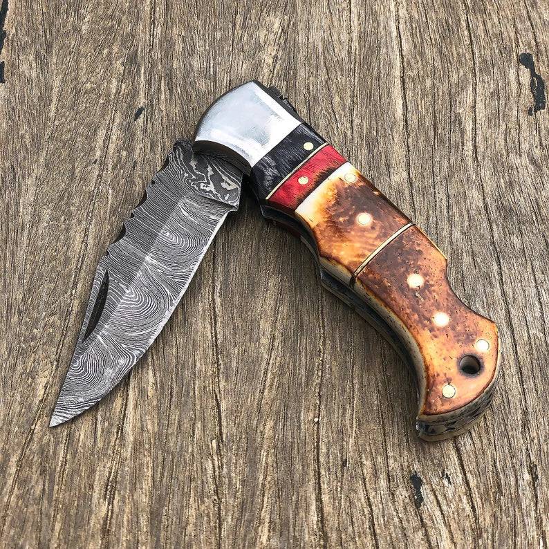 Damascus folding pocket knife with burnt camel bone handle, handmade by cskforged, showcasing intricate Damascus steel patterns.