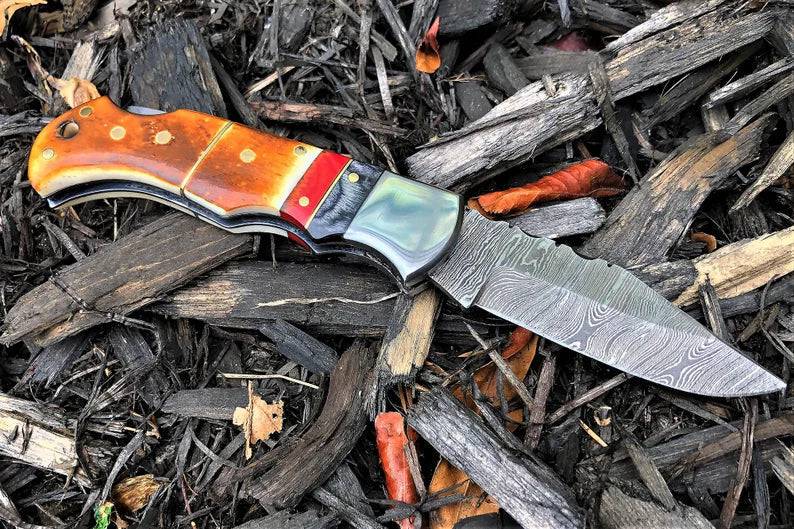 Handmade Damascus folding pocket knife with burnt camel bone handle by cskforged, showcasing intricate steel patterns and natural wood tones.