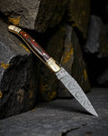 Damascus steel folding pocket knife by cskforged with handcrafted brass accents and exotic wood handle, open blade visible.