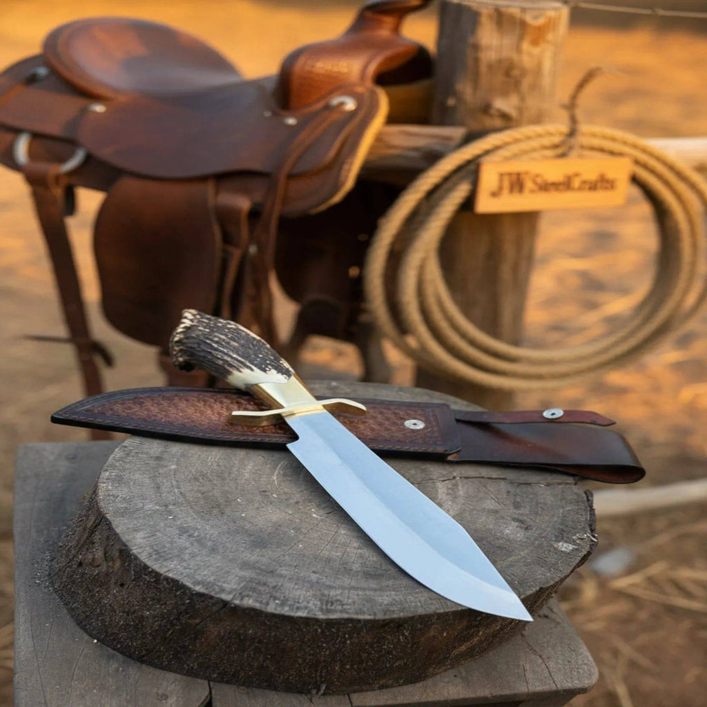 Handmade JW SteelCrafts carbon steel hunting knife with stag horn handle and leather sheath, displayed on a wooden surface.