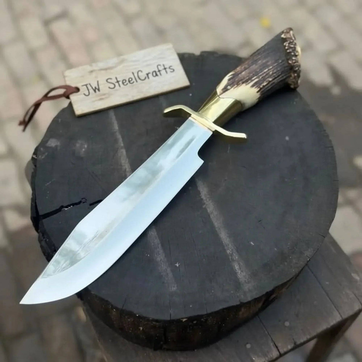 Handmade JW SteelCrafts carbon steel hunting knife with stag horn handle and leather sheath, displayed on a wooden surface.