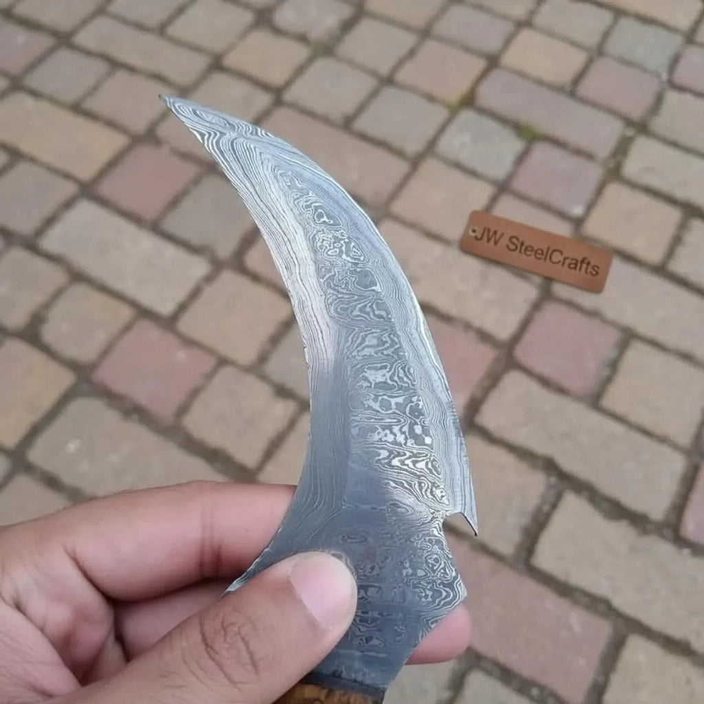 Damascus steel JW SteelCrafts karambit knife with curved blade and textured handle, showcasing craftsmanship and detailed design.