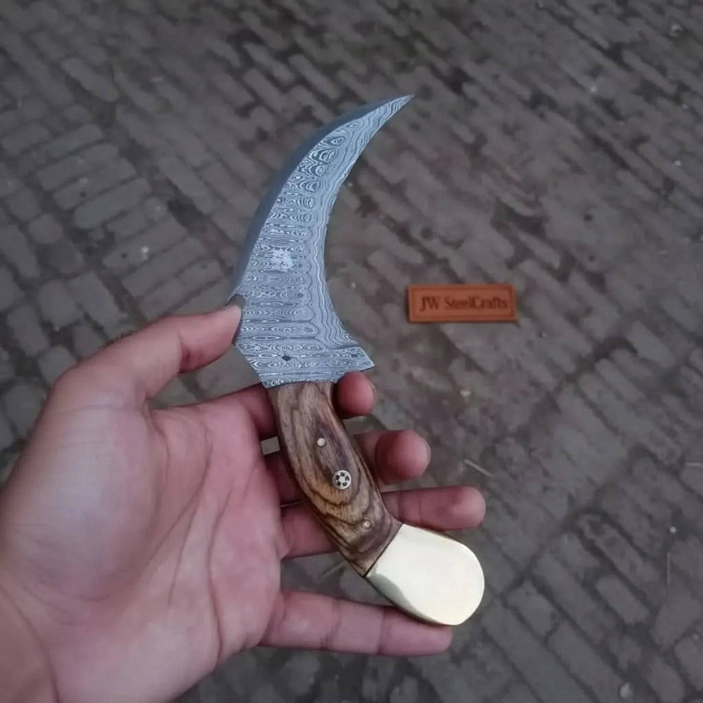 Damascus JW SteelCrafts karambit knife with curved blade and textured handle, showcasing intricate Damascus steel pattern.