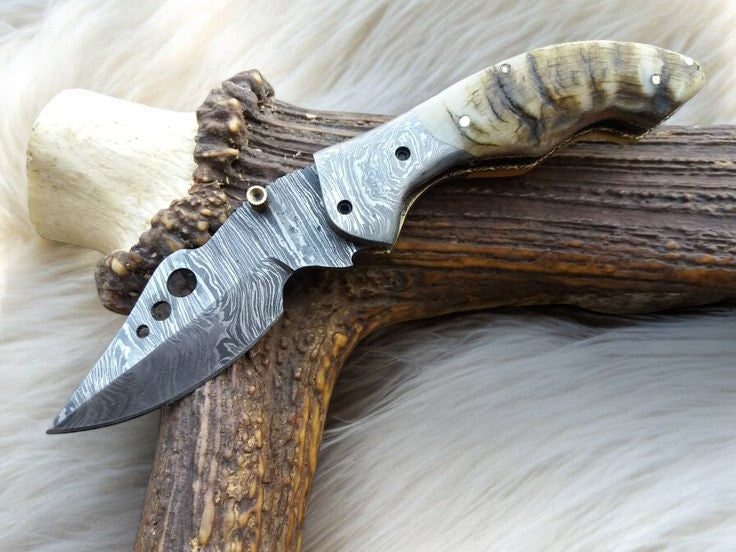 Handmade Damascus pocket knife with a sheep horn handle, featuring intricate metalwork and a sleek, compact design.