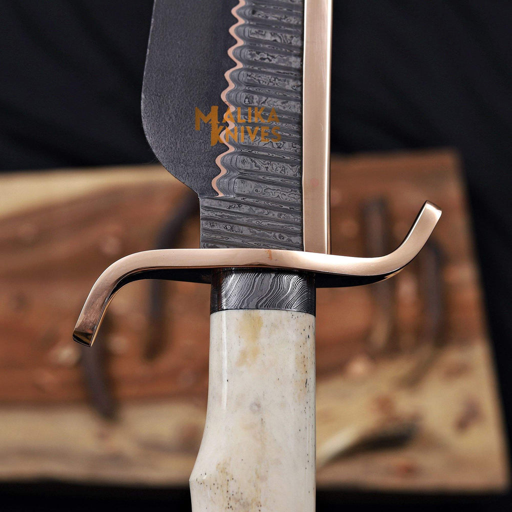 Close-up of the Copper Damascus Alamo Musso Bowie Knife by MALIKA KNIVES, showing the copper guard, pommel, and Damascus blade details.