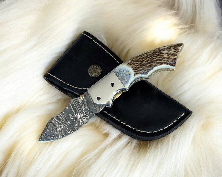 Custom handmade Damascus pocket knife with stag horn handle, featuring intricate blade pattern and durable craftsmanship.