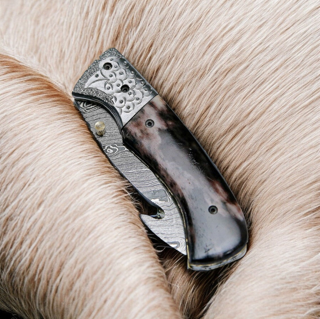 Custom handmade Damascus pocket knife with a colorful bone handle, featuring intricate blade patterns and a compact design.