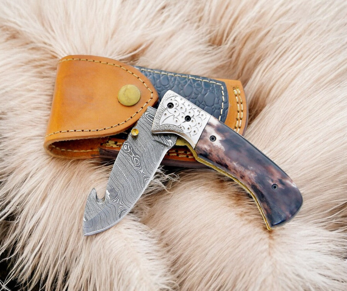 Custom handmade Damascus pocket knife with a colored bone handle, featuring intricate blade patterns and a polished finish.