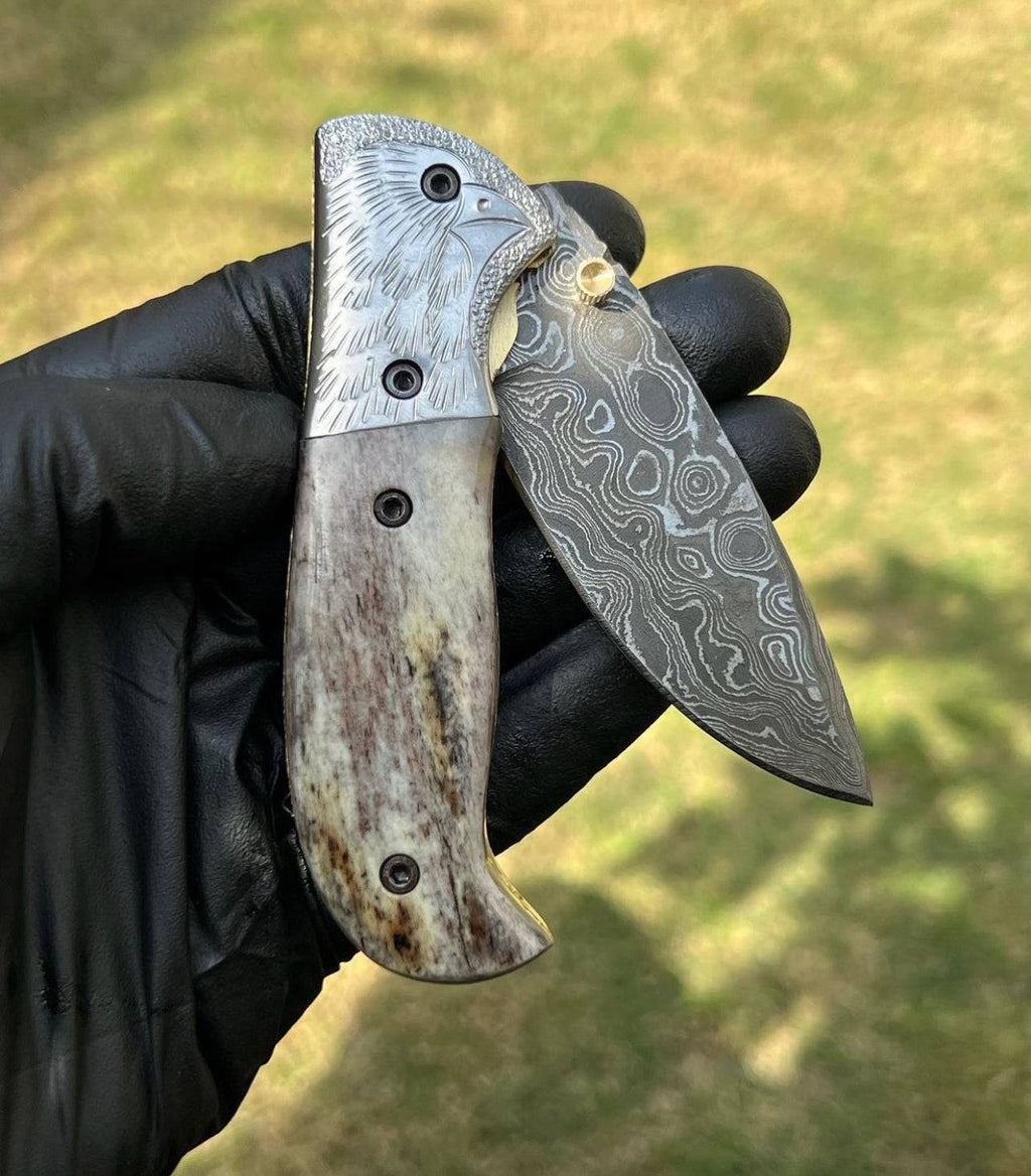 Damascus pocket folding knife by cskforged with a patterned blade and ergonomic handle, displayed in a partially open position.