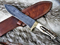 Handmade Damascus steel stag horn hunting knife with leather sheath from Knives Gear Garage, showing the detailed blade and rustic handle.