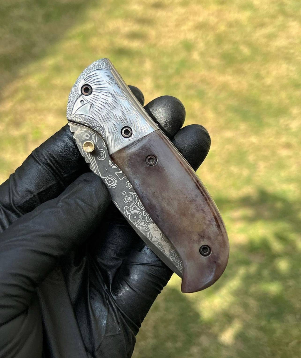 Damascus pocket folding knife by cskforged with a patterned blade, stainless steel handle, and a secure locking mechanism.