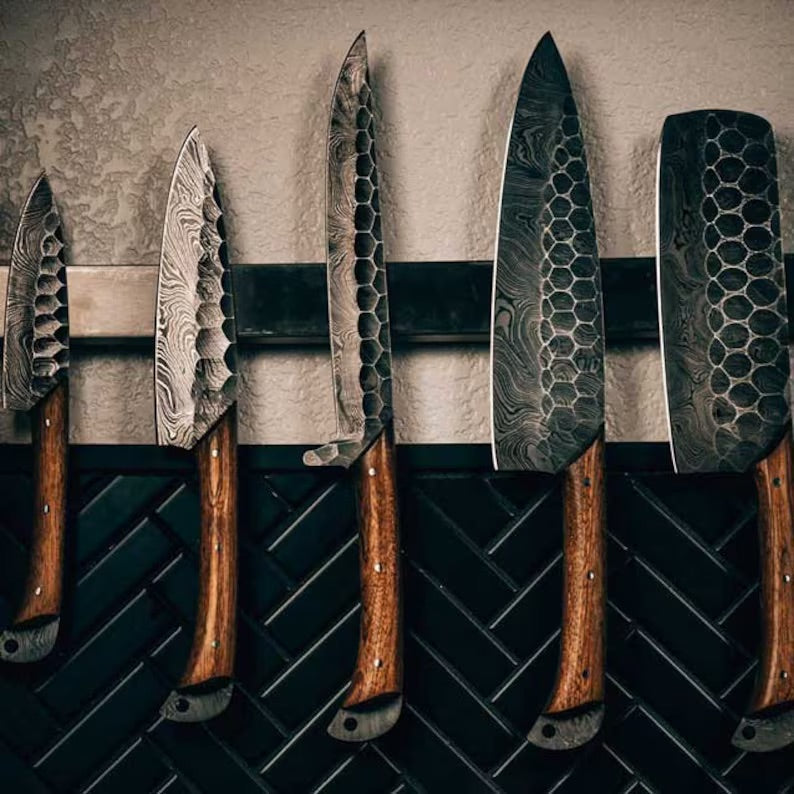 Handmade Damascus kitchen knives set with rosewood handles in a leather roll kit, showcasing craftsmanship and natural wood grain.