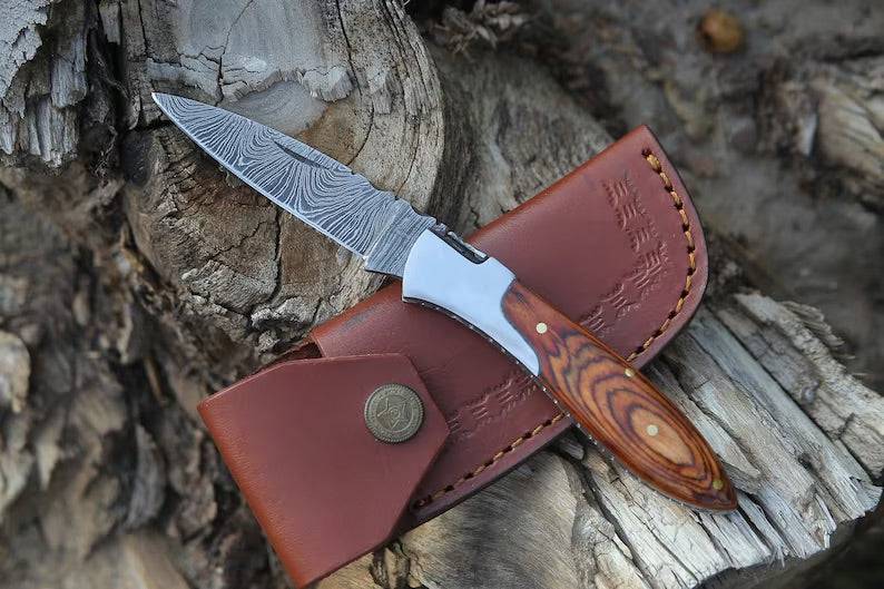 Handmade Damascus pocket knife with brown Pakka wood handle by Knives Gear Garage, featuring a folding blade and intricate pattern.