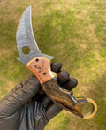 Damascus folding pocket knife with karambit design by cskforged, showcasing intricate blade patterns and ergonomic handle.