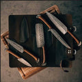 Custom handmade Damascus kitchen knives set with rosewood handles displayed in leather roll kit by Knives Gear Garage.