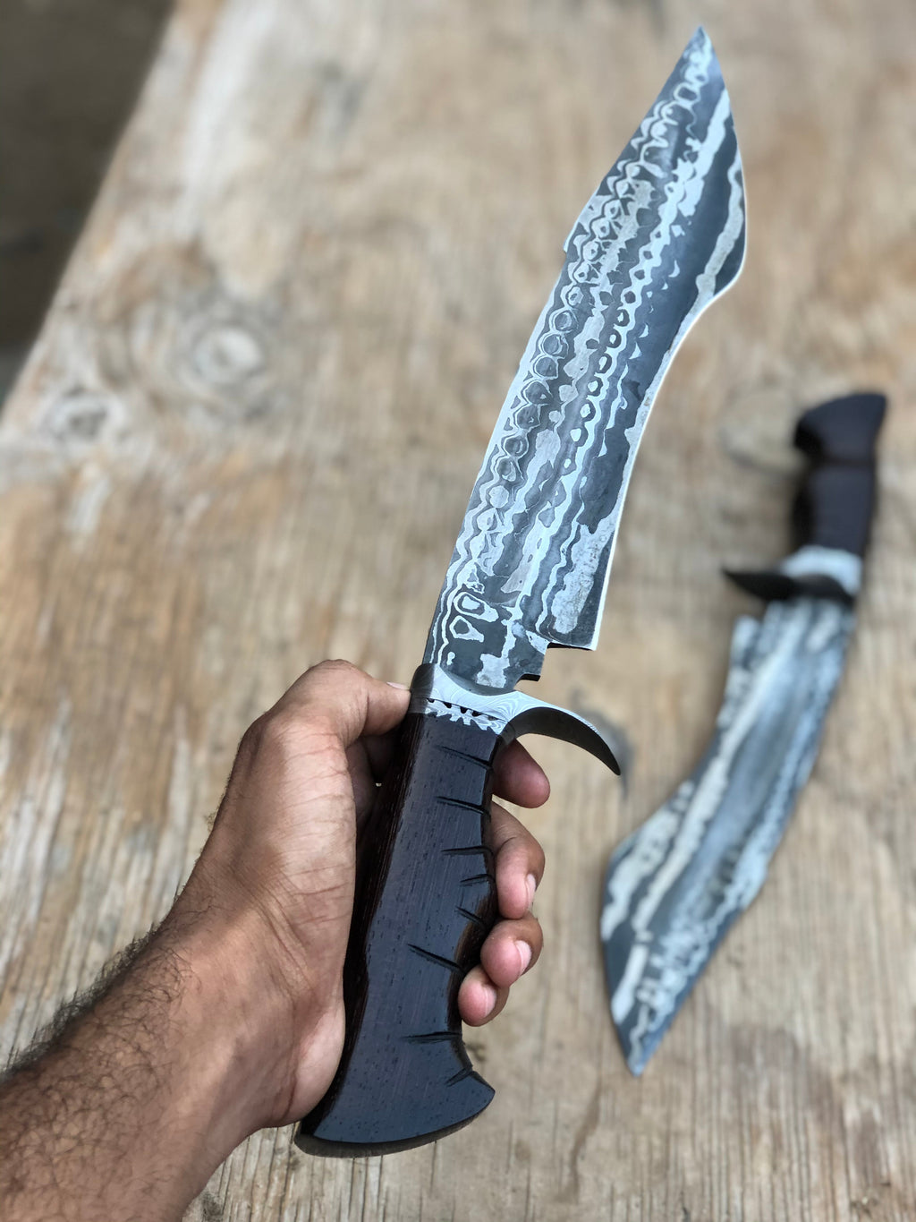 Custom handmade Damascus steel hunting Bowie knife with a leather sheath, featuring intricate patterning and a sturdy handle.