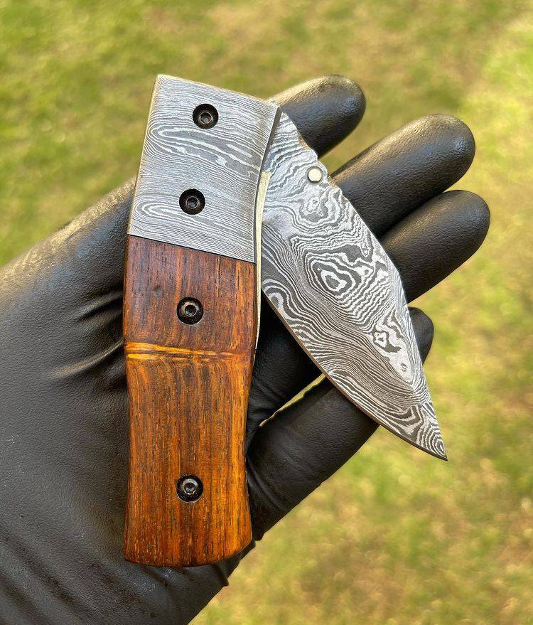 Damascus folding EDC pocket knife by cskforged with a polished blade and textured handle in a closed position.
