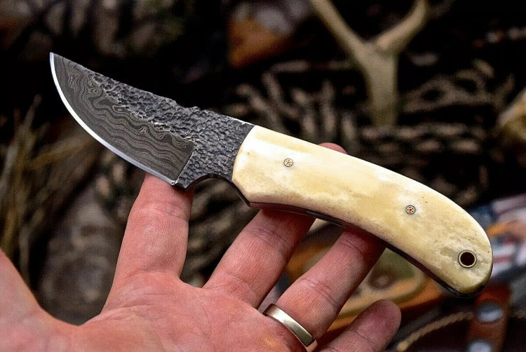 Handmade 7-inch Damascus steel deer skinning knife with camel bone handle and leather sheath, perfect for hunting and field dressing.