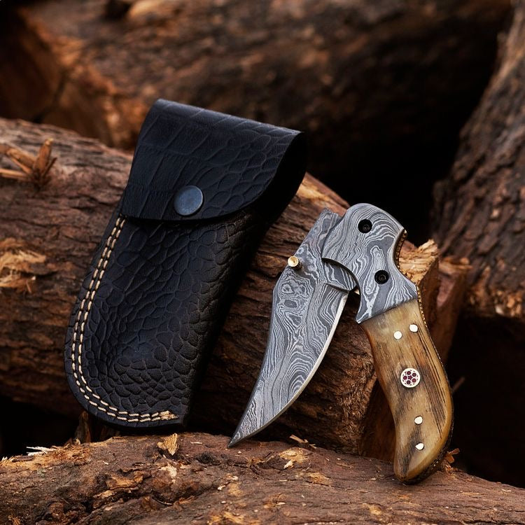 Damascus steel folding knife with textured handle and sharp blade, made by Knives Gear Garage, displayed open on a wooden surface.