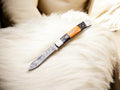 Handmade Damascus pocket knife with exotic wood handle and bone accents, showcasing intricate blade patterns and craftsmanship.