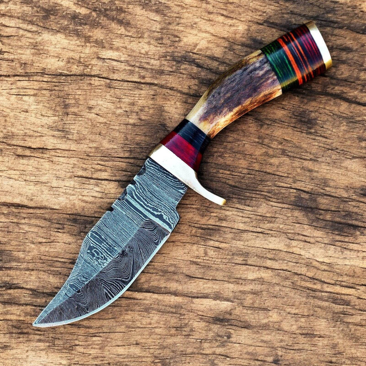 Handmade Damascus hunting knife with a polished blade and antler horn handle, displayed on a wooden surface.