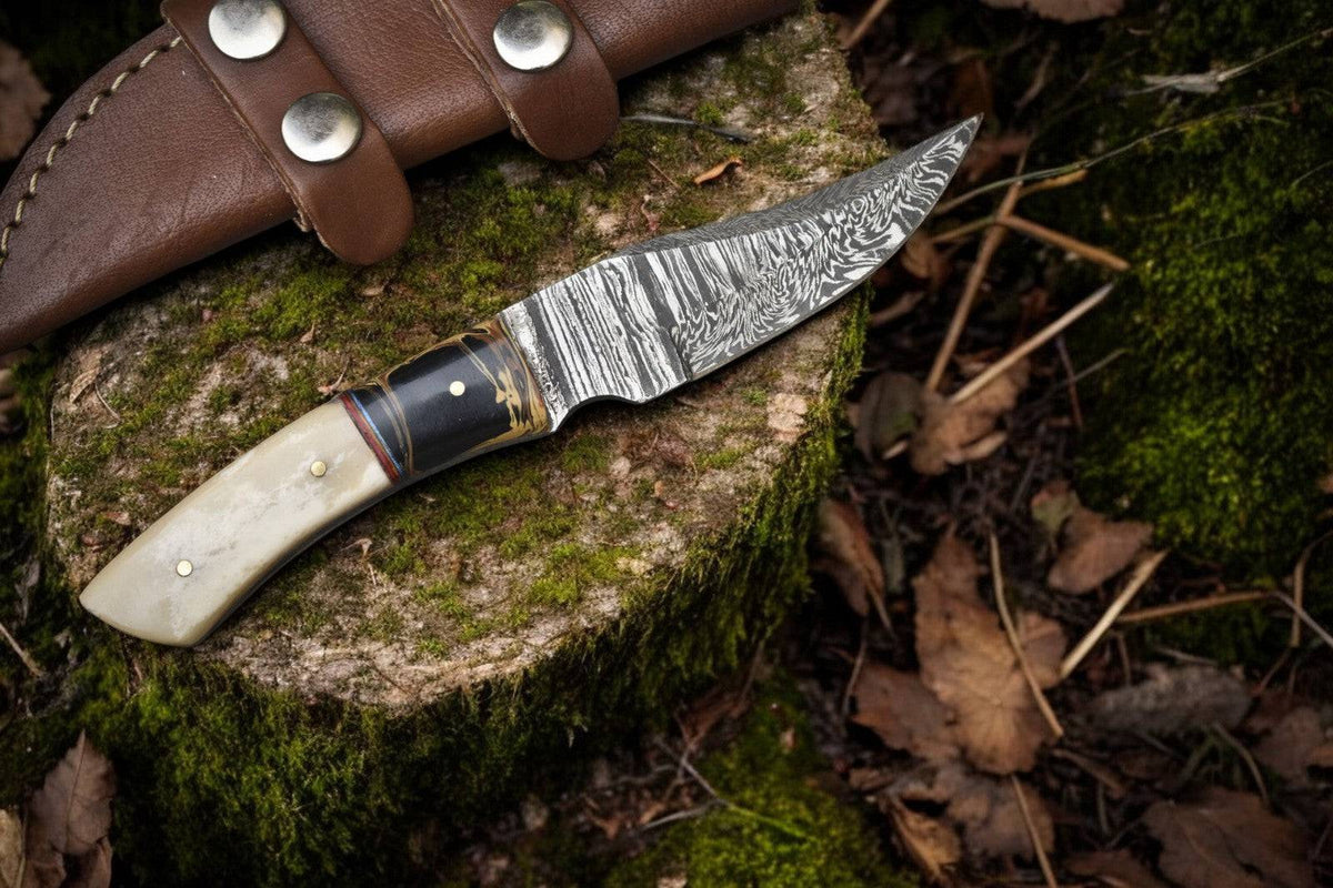 Handmade Damascus skinning knife with epoxy resin handle and bone accents, featuring a sharp stainless steel blade.