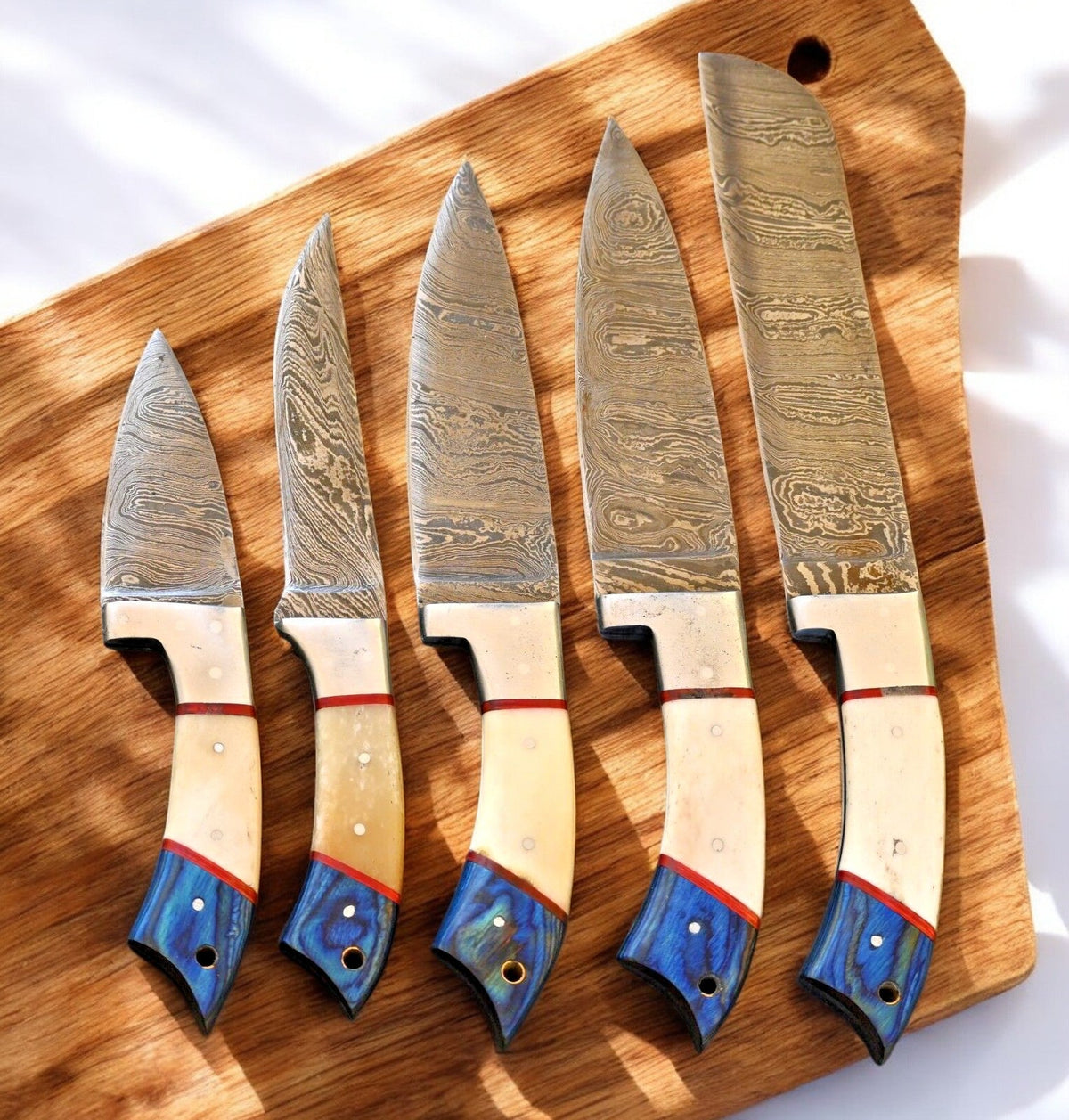 Handmade Damascus kitchen knives set with exotic wood and bone handles, displayed on a wooden cutting board.
